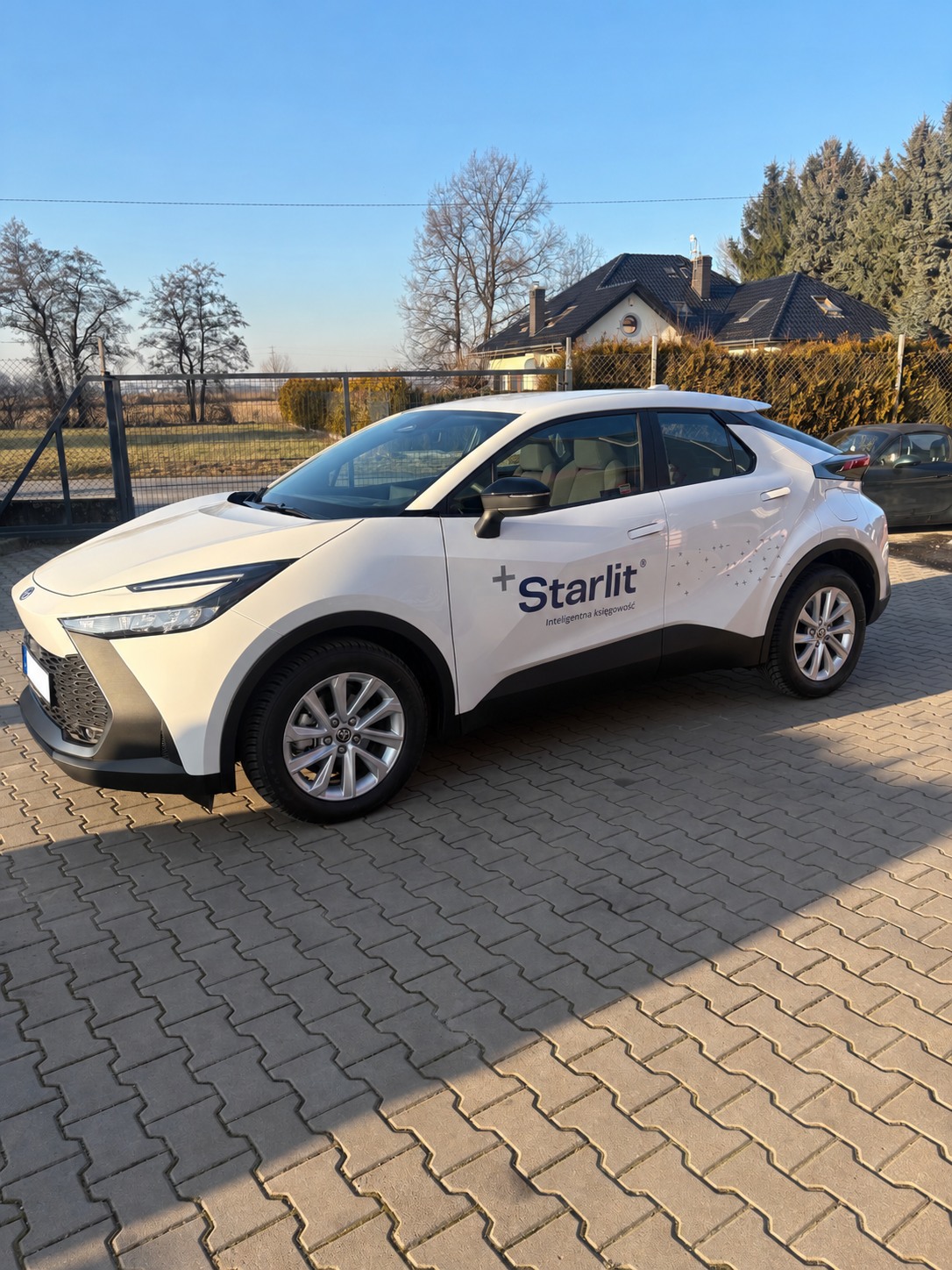 Biała Toyota z logo Starlit na drzwiach zaparkowana przed budynkiem