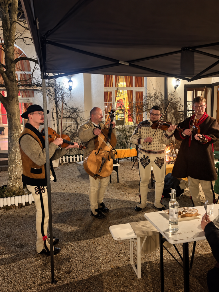 Czterech muzyków gra na skrzypcach i wiolonczeli pod zadaszeniem.